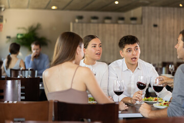 Two couples of men and women drinking eating and talking in restaurant