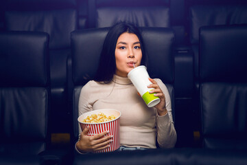 Motion picture fun. Cute Asian girl with popcorn and drink in cinema
