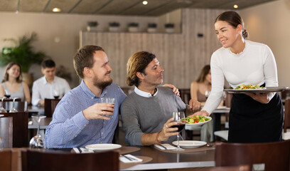 Young woman waitress takes order from couple young man and adult man in restaurant..