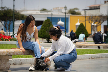 Young woman helping friend putting on inline skates in city park