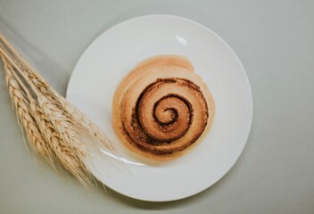 Fresh close-up cinnabon on a plate on a gray background with wheat for a cafe