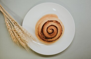 Fresh close-up cinnabon on a plate on a gray background with wheat for a cafe