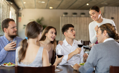 Obraz premium Young female waitress takes order from group of male and female friends in restaurant