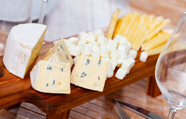 Cheese appetizer is prepared on serving board - assorted varieties, sliced mature cheese, cubes and large pieces of mold-ripened cheese, and cheese balls.