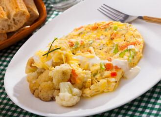 Vegetable omelet with garnish of baked cauliflower sprinkled with grated cheese on white plate..