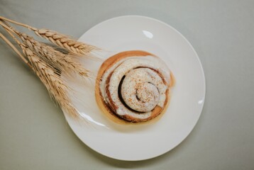 Fresh close-up cinnabon with butter cream on a plate on a gray background with wheat for cafe