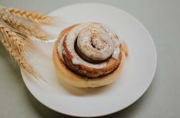 Fresh close-up cinnabon with butter cream on a plate on a gray background with wheat for cafe