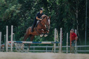 A skilled equestrian rider gracefully navigates a jump on a powerful horse during a competitive...