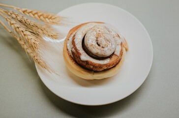 Fresh close-up cinnabon with butter cream on a plate on a gray background with wheat for cafe