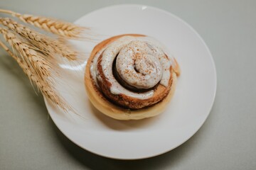 Fresh close-up cinnabon with butter cream on a plate on a gray background with wheat for cafe