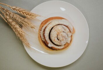Fresh close-up cinnabon with butter cream on a plate on a gray background with wheat for cafe