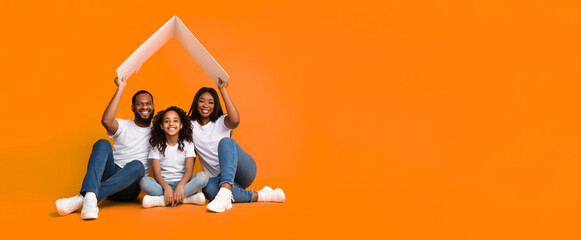 Family Housing And Insurance. Smiling black parents holding conceptual cardboard roof above happy...