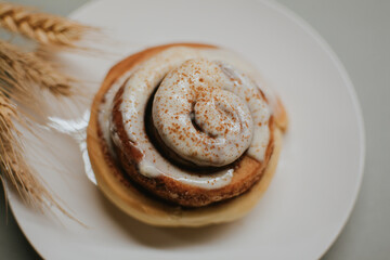 Fresh close-up cinnabon with butter cream on a plate on a gray background with wheat for cafe