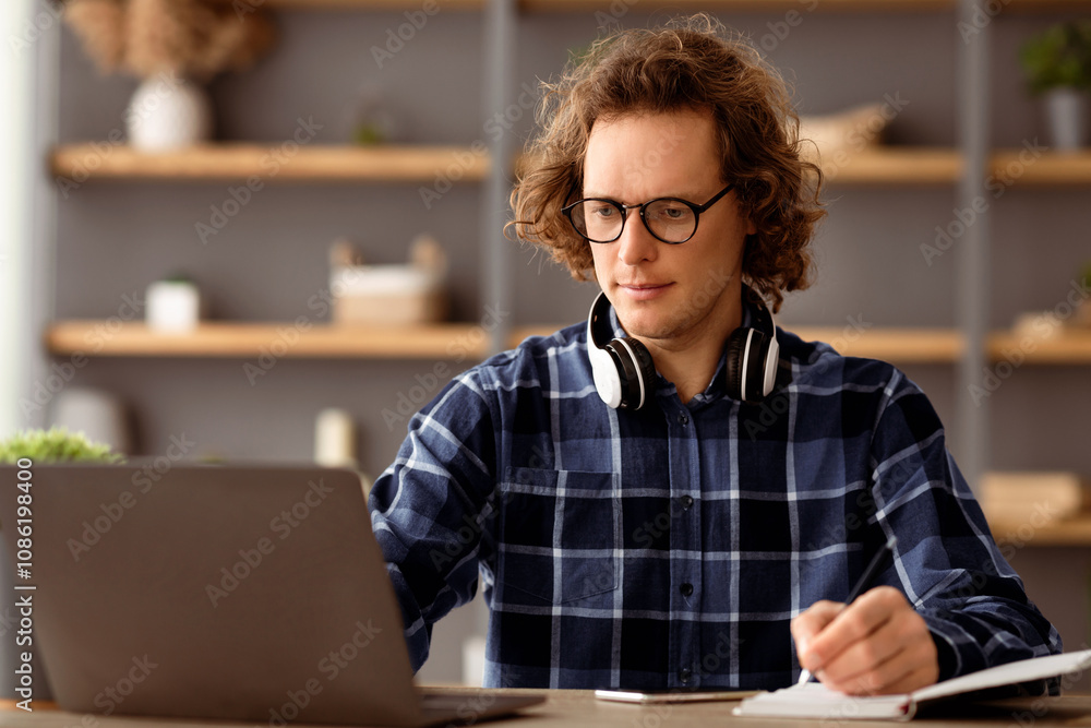 Poster serious businessman taking notes writing business report checking online data using laptop working s