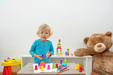 Cute little child boy having fun at home playing with colorful stamps on paper. Educational indoor activity for kids.