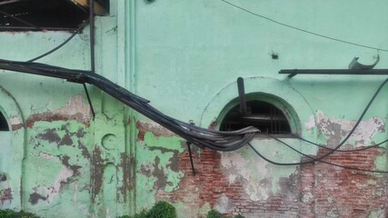 Exterior of an old factory building with peeling green paint, exposed bricks, and tangled cables...