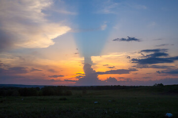 Cumulus clouds against a bright sunset with rays of light on the horizon.