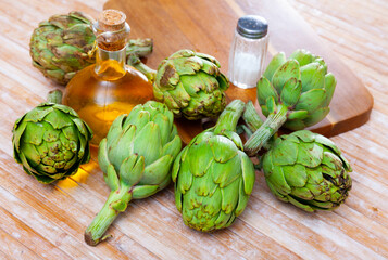 Raw ripe green artichokes, salt and olive oil on wooden table, ingredients for cooking at home