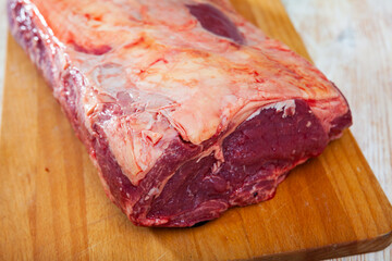 Large raw piece of beef tenderloin on wooden cutting board on light background