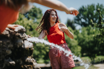 Friends having fun and splashing with water at the fountain on a hot summer day, enjoying the...