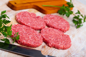 Raw meat cutlets with parsley on wooden cutting board