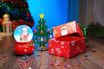 Open Christmas Gift Box Next to a Festive Christmas Tree and a Glass Snow Globe with Santa Claus Inside. Perfect Scene for Christmas and New Year Greetings. Box Contents Editable in a Photo Editor.
