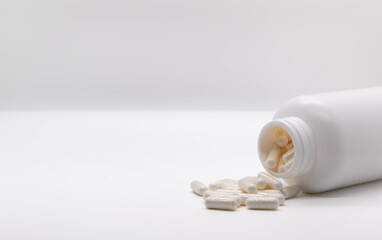 Shot of white pills coming out of a white plastic bottle in the lower right corner. Copy space. Medicine and health concept. selective focus