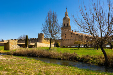 View of tall Gothic bell tower of Cathedral in Burgo de Osma surrounded by ancient fortifications walls on sunny spring day. Historical religious monument of Spanish province of Soria