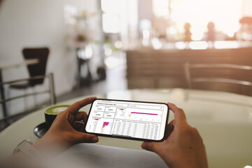 Person analyzing corporate spending dashboard on smartphone at cafe, displaying financial charts, graphs and data metrics while enjoying matcha latte, device held horizontally with sunlit background.