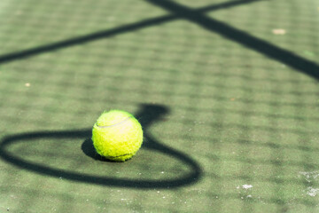 A close up of a tennis ball tennis ball with a racket shadow on a hard court in the morning