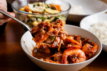 Spicy shrimp soup in a white bowl on a wooden table, udang balado,