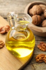 Cooking oil in jug and walnuts on wooden table, closeup