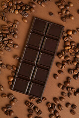 Tasty chocolate bar and coffee beans on brown background, flat lay