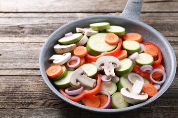 Frying pan with mix of fresh vegetables and mushrooms on wooden table, closeup
