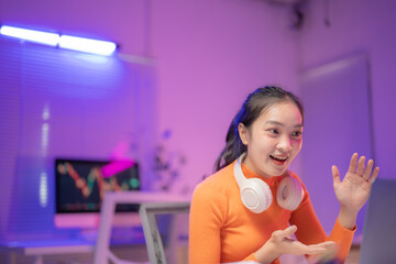 Asian businesswoman in a stylish purple office at night, focused on a video call, gesturing and working on her laptop, showcasing modern communication