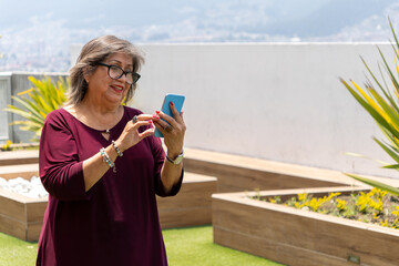 Senior Latina woman looking at her cell phone smiling in the garden