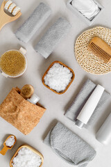 Natural spa, wellness, bath accessories as minimal flat lay pattern, sea salt flakes in wooden bowls, soft gray towels, brush, reusable cotton pads, grey conctrete background, top view neutral colors