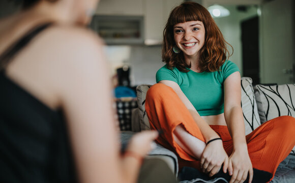 Bright and cheerful woman with red hair and casual attire, happily engaged in a friendly conversation at home. The setting exudes warmth and connection between friends.