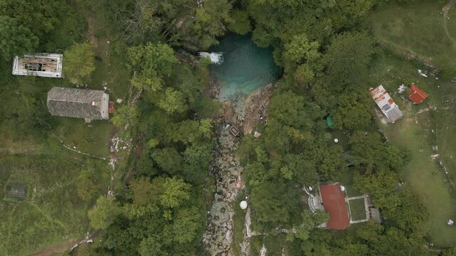 Albania's blue eye spring and surrounding forest landscape with small rural buildings, aerial view