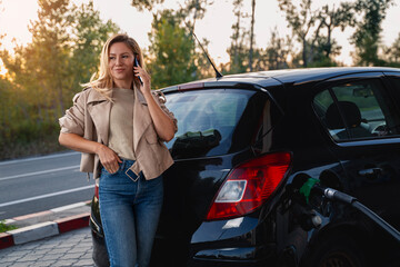 Young woman filling up gas tank of her car, at sunset