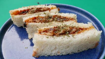 group of sliced ​​bread with meat filling, fried onions on a blue plate, green background