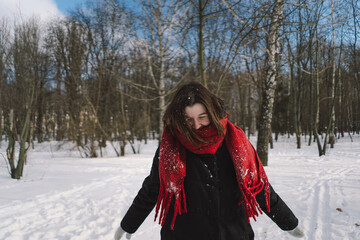 A smiling woman with a red scarf enjoys a snowy winter day in a serene forest setting beneath a...