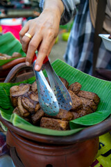 The gudeg seller is picking up bacem tempeh using tongs