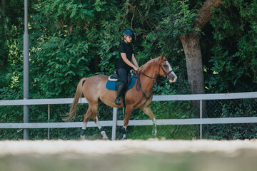 Person riding a chestnut horse in an outdoor equestrian arena, surrounded by lush green trees.