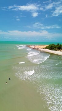 Clear turquoise waters along Jericoacoara Beach, Brazil, with gentle waves and white sand crashing along past people playing in water, Vertical