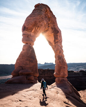 Woman walking towards Delicate Arch underneath the sun flare Arches National Park