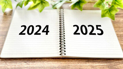 開いたリングノートに2024と2025文字_茶色板背景正面