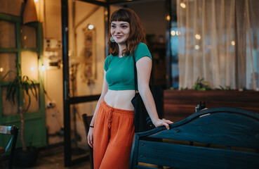 A cheerful young woman with modern fashion stands in a cozy, stylish indoor cafe. The setting...