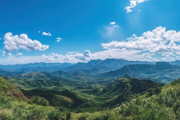 A panoramic view of a vast, rolling mountain range under a clear blue sky with fluffy white clouds.