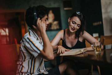 A young man wearing headphones and a woman reading a book share a relaxed study session in a cozy coffee shop environment, fostering learning and connection.